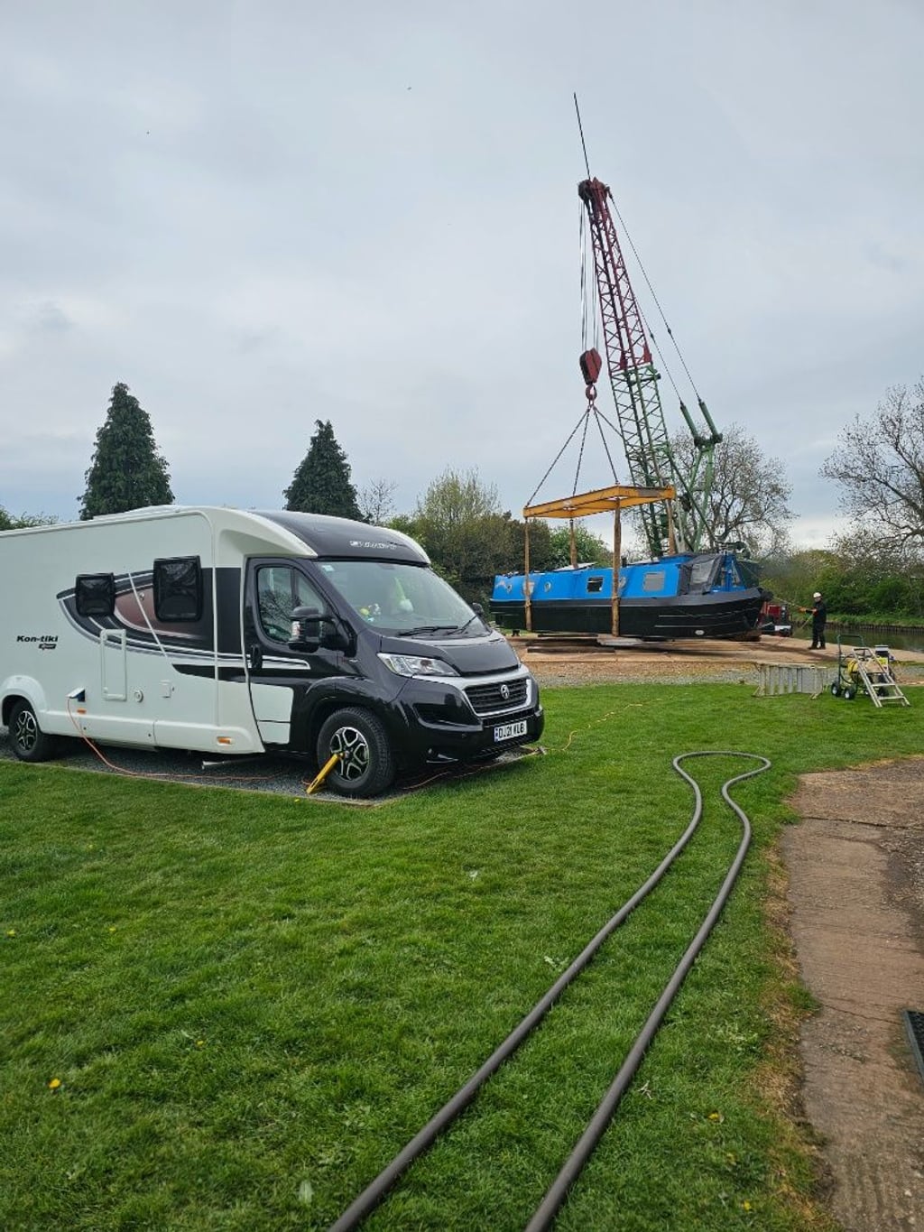 The motorhome pitched beside a canal marina where a narrowboat is being craned into the water