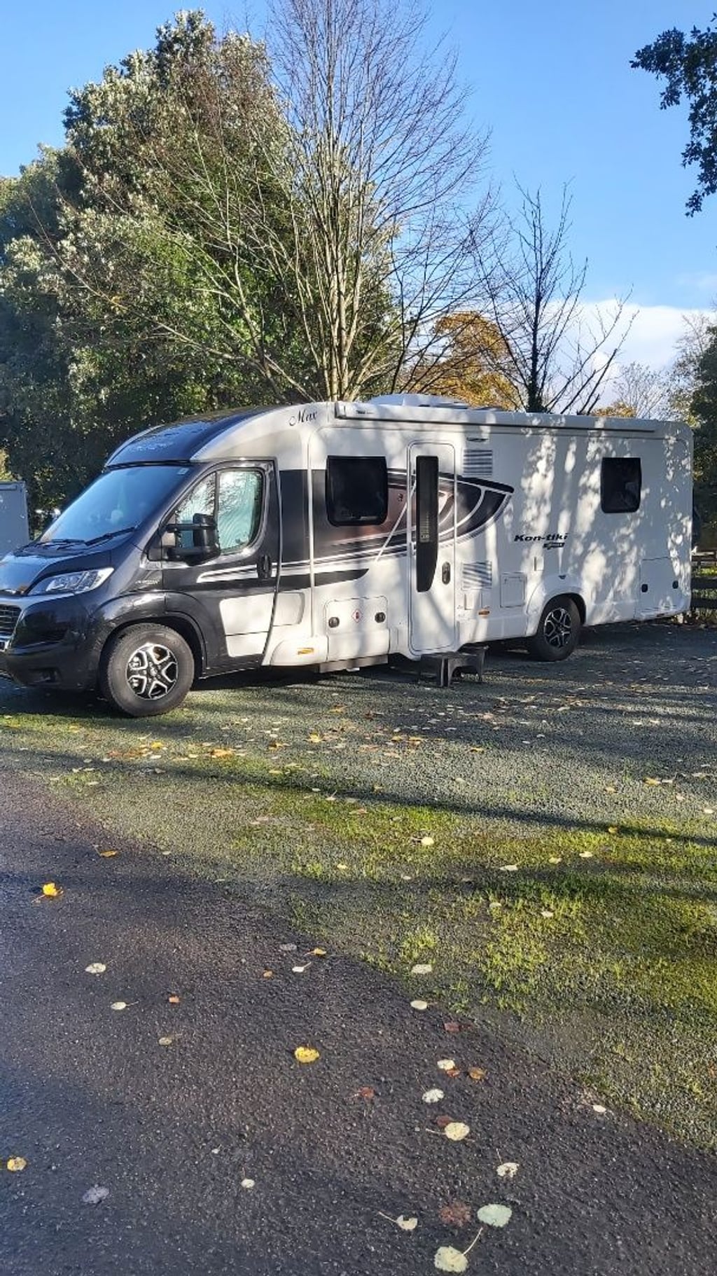 Side profile of the white Swift Kon-Tiki Sport 599 motorhome parked on a gravel pitch among autumn trees